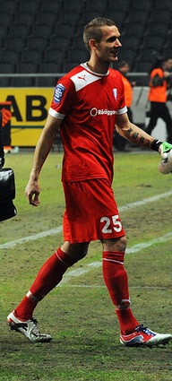 A photograph of a man wearing a red football shirt, red shorts and red socks.