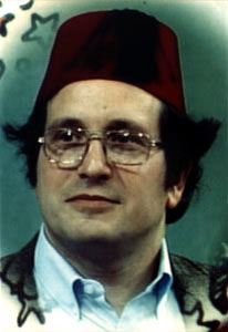 Photograph of head of a man wearing glasses and a dark burgundy fez hat