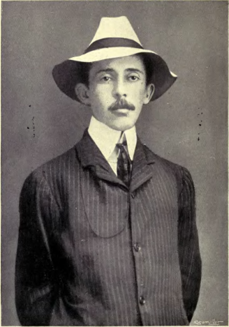 Santos-Dumont standing with his hands behind his back in a suit and hat