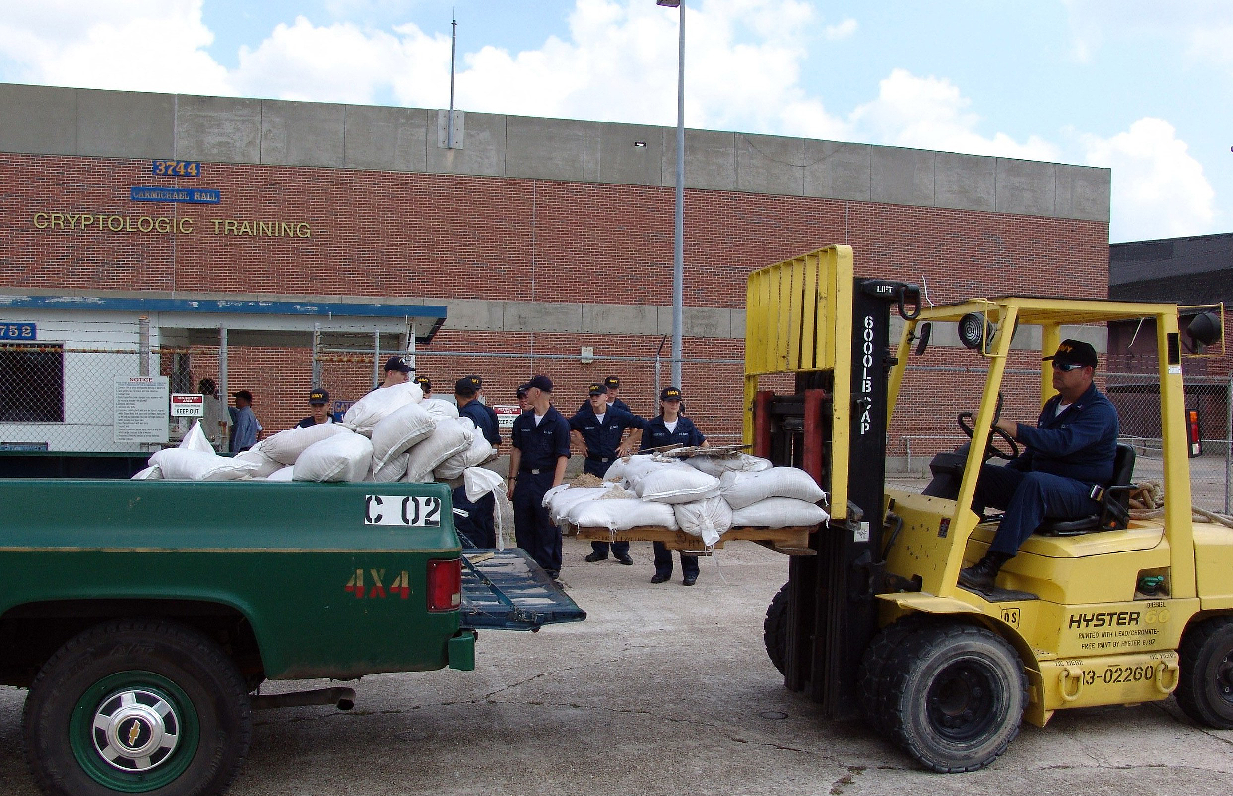 US Navy 050708-N-9246G-016 Cryptologic Technician 1st Class Henry Hughes unloads pallets of sand bags at the Center for Information Dominance, Corry Station, as awaiting Sailors prepare to place them around exterior doorways.jpg