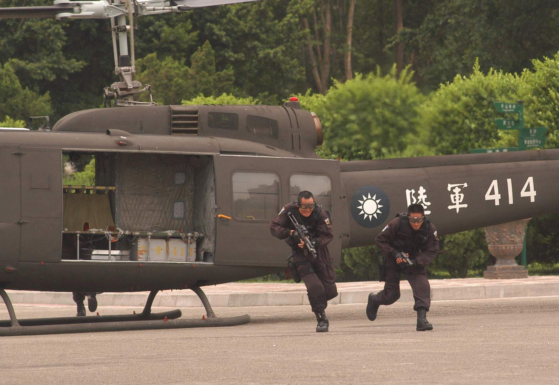 Two men in military uniform getting off an helicopter. They are both running and carrying a weapon.