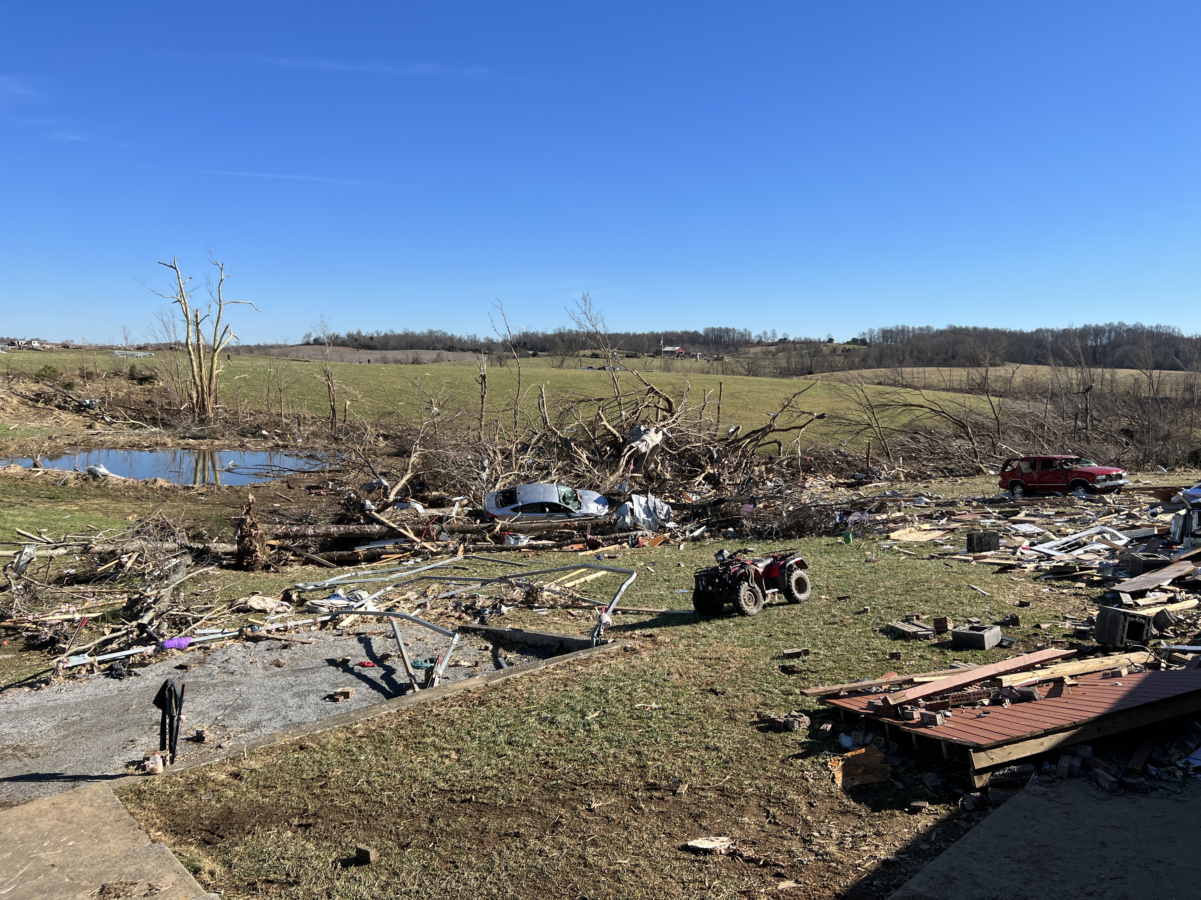 The remnants of a completely destroyed home strewn into a pond and nearby trees along with two destroyed vehicles near Saloma, Kentucky.