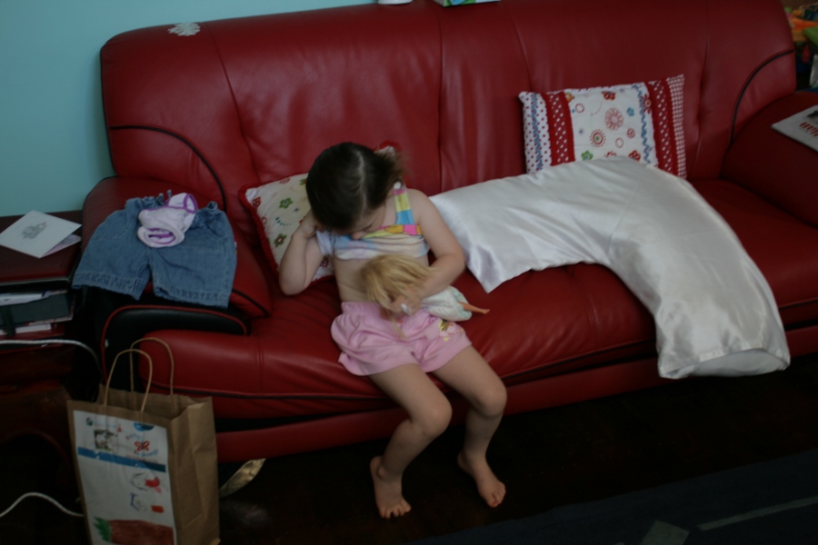 Girl nursing her doll on a red couch.