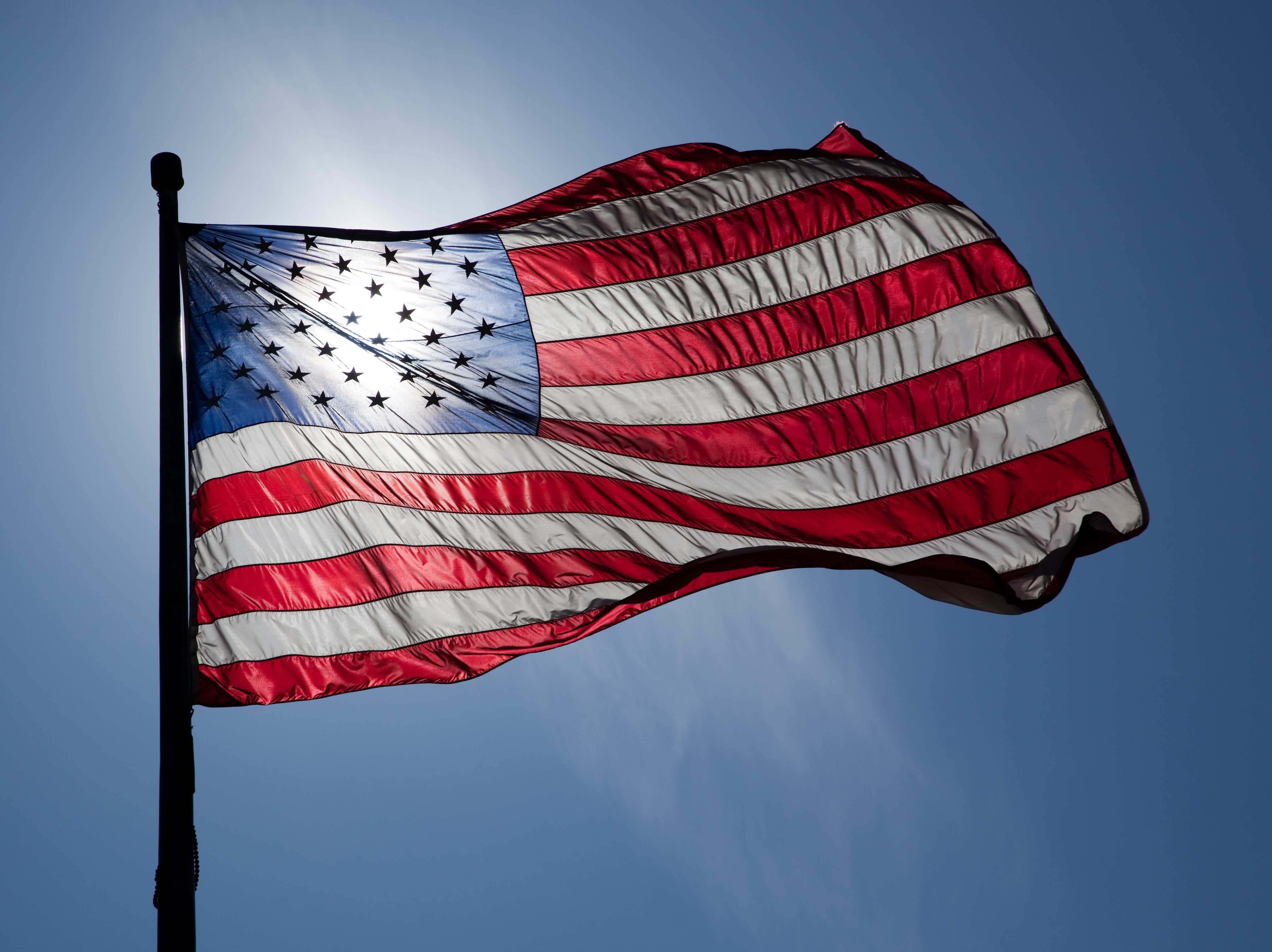 American flag flying with sun behind it