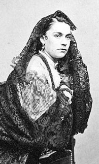 A young white woman posing in a costume of dark fabric and lace; she has dark hair.