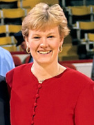 Zdjęcie portretowe. Uśmiechnięta kobieta z krótko obciętymi, blond włosami. Na uszach nosi okrągłe kolczyki. Ubrana jest w czerwoną bluzkę zapinaną na guziki.