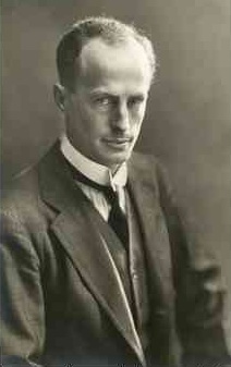 Man, mid-thirties, receding hair, clean shaven, wearing a high collar with tie. He is facing half right but his eyes are on the camera.