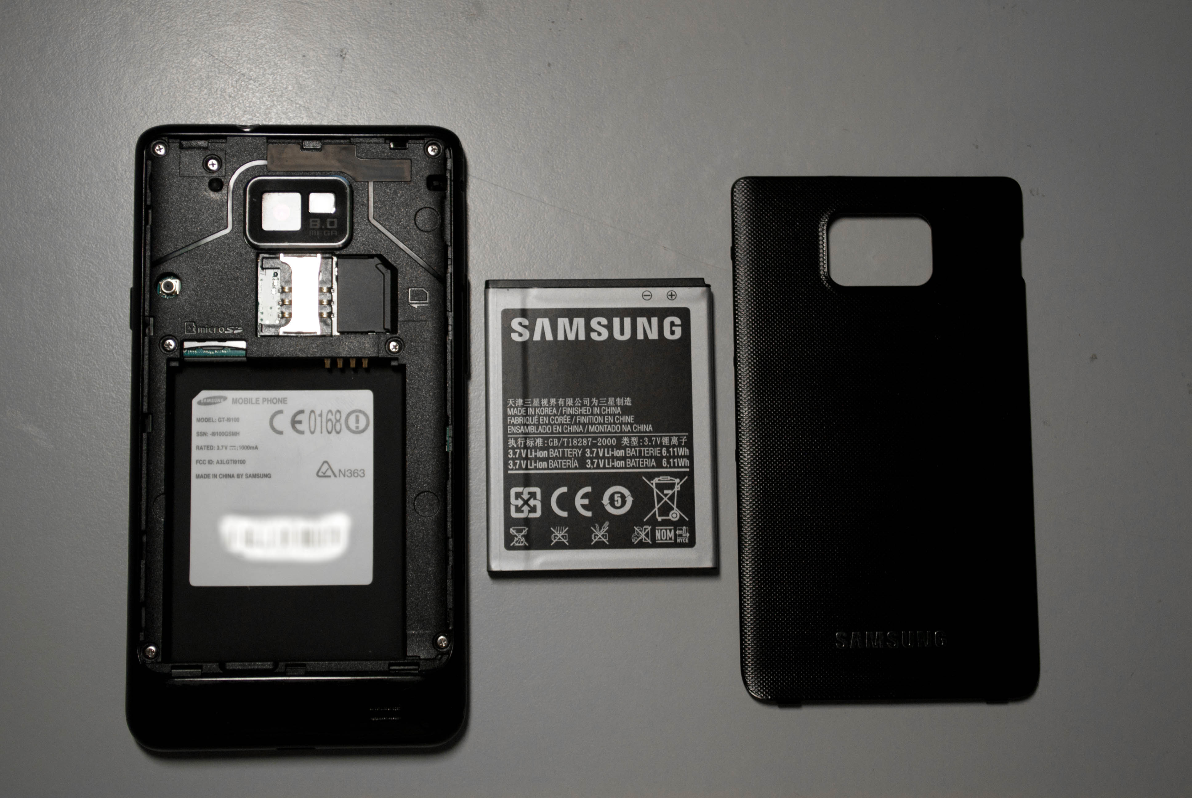 Dismantled Samsung Galaxy S II, from left to right components include the handset, battery and back cover