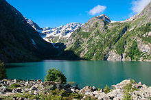 Lac aux eaux turquoises dans un vallon où se mêlent rochers, verdure et névés.