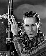 A black-and-white photo of country singer Chet Atkins, holding a guitar upright.
