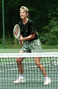 En lyshåret kvindelig tennisspiller med flerfarvet shorts og en sort top med sin tennisketcher.