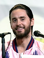Frontal picture of a young man with green eyes and beard, behind microphones.