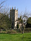 Stone building with prominent square tower. Surrounded by trees and with green grass area in the foreground separated from the building by a stone wall.