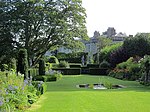 a lawn with surrounded by trees and plants, there is a large house in the background