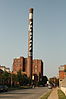A tall, brown brick smokestack displays the word "FALSTAFF" down its side and stands to the left of a street.