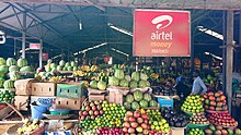 Interior photograph of the market, showing fruit available for sale as well as a hoarding advertising Airtel