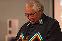 Photo of Justice Murray Sinclair during opening keynote. He is seen, while looking down and smiling, wearing a black top with multi-coloured accents.