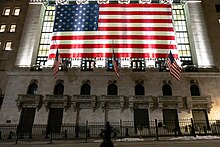 The statue (bottom) in its current location: facing the New York Stock Exchange Building The fearless girl takes on NYSE (47406406981).jpg