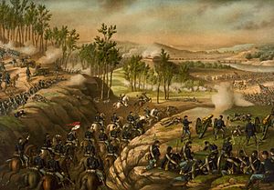 A photograph of Union cavalry moving through a gap to attack Confederate infantry, with Union foot soldiers and cannons firing at the Confedereates on either side of the ridge