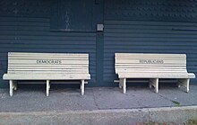 Two benches, one carved with "DEMOCRATS" and one with "REPUBLICANS", in front of a building