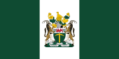 A flag bearing three equally-wide vertical stripes, green, white, and green, with a coat of arms prominently emblazoned on the centre of the middle stripe.