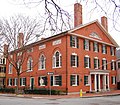 A large rectangular two story hall made of brick. The long side has five large windows topped with a rounded window section, while the short side has more conventionally sized windows.