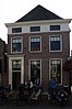 Hoekpand Rozemarijnsteeg. Huis met hoog schilddak. Voorgevel met lijst, parterre, verdieping en mezzanino. Deuromlijsting met pilasters. Achtergevel met vlechtingen. De hoge achterpuntgevels van de panden 13 en 15 vormen een monumentale afsluiting van de Rozemarijnsteeg.