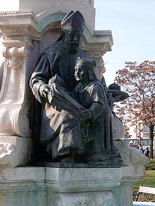 Statue en bronze représentant un évêque assis faisant la lecture un enfant portant une couronne.