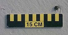 Koule dehtu široká asi 1 cm na písku nad měřítkem 15 cm
