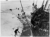 Men with digging tools removing ice surrounding the ship's hull, creating an icy pool of water