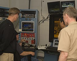 An engineering technician explains instrument readings. US Navy 091013-N-4288H-006 Engineering Technician Wayne Wood, second from the left, explains instrument readings from a biofuels test on an F404 engine from an F-A-18.jpg