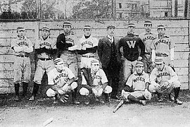 Photo d'une équipe de baseball. Les sportifs sont addosés à un mur, les bras croisés, et en grandes lettres, est inscrit le nom de leur université : « Waseda » ou juste « W ».