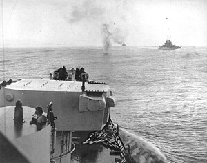 Сбитый японский самолёт (вверху по центру) падает в океан рядом с американским крейсером Колумбия 2 ноября 1943 года во время воздушной атаки кораблей Союзников у Бугенвиля через несколько часов после морского сражения в заливе Императрицы Августы.