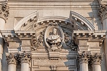 Sculpture en marbre représentant un homme en habit religieux blanc avec ornements en marbre autour sur le portique d'un édifice