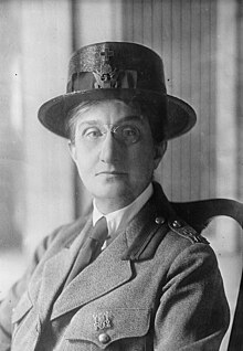 A middle-aged white woman wearing a brimmed cap and a uniform with shirt and tie