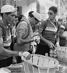 Photographie en noir et blanc d'un cycliste portant des gants et une casquette à la visière relevée en train de remplir une musette.