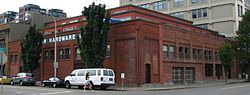 Photograph of a section of the Honeyman Hardware Company Building, a two-story, brick warehouse building on a city street corner, with recessed, modern residential levels on the roof