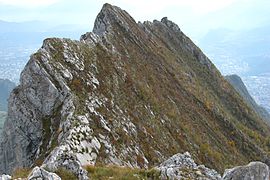 Arête rocheuses avec des falaises à gauche et un versant très incliné avec une végétation basse à droite.