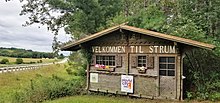 a sign in the shape of a quaint Scandinavian-looking cottage, with words reading "Welkomen til Strum"
