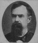 Black and white photo shows a heavily bearded man in civilian clothes.