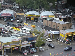 A series of auto parts and repair shops, littered with junked cars and lined with tires for sale.