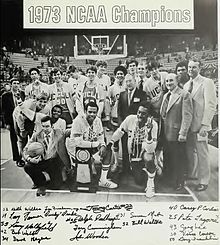 A black-and-white photograph of the 1972–73 UCLA Bruins men's basketball team posing with the NCAA championship trophy