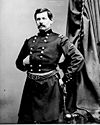 Man with moustache in uniform with two vertical columns of buttons with left hand on hip and right hand tucked inside uniform