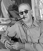 Foto hitam-putih John Ford sedang merokok pipa.