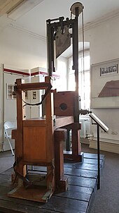 Guillotine, Baujahr 1946 und im Ausstellungsraum des Museums stehend, besteht aus einer Holzbank mit vorgelagertem Schlitten, auf dem der Verurteilte fixiert, in die Horizontale gebracht und mithilfe von auf der Unterseite befestigten Rollen auf der Holzbank nach vorne bis zum Kopfteil gezogen wird. Kopfteil besteht aus einer hölzernen Halskrause, die angehoben werden kann, einem Auffangbehältnis für den Kopf und einem circa drei Meter hohem Eisengerüst, an dem das, an einem Gewicht befestigte Fallbeil hängt, dass durch einen Hebel an der Seite des Kopfteils gelöst wird, als Objekt im Strafvollzugsmuseum ausgestellt