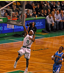 Rondo réalisant un dunk sous les yeux d'un joueur de l'équipe adverse.