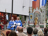 A modern replica of the statue shown above processes through Ravensburg, above a modern model of the old city