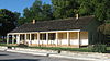 A wooden house with gabled roof and a broad porch, highlighted by the afternoon sun