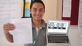 The logo on the screen in the subject's left hand is a Creative Commons license, while the paper in his right hand explains, in Khmer, that the image is open content Discussing Creative Commons licensing in Khmer.jpg