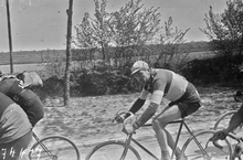 Photographie en noir et blanc montrant un cycliste en course au sein du peloton.